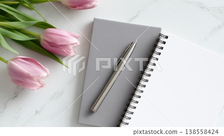 一張白色桌上放著一本打開的筆記本、一支筆和一朵鬱金香。 138558424
