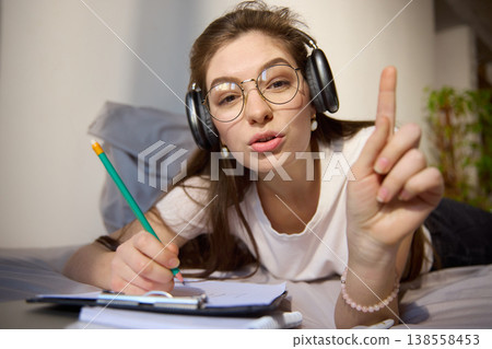 Young woman with headphones pointing finger during online lesson at home Young woman with headphones pointing finger during online lesson at home 138558453
