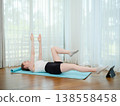 Young woman doing core exercise at home on yoga mat. Concept of fitness, strength training, and online workout. Female performing alternating leg raise while following virtual class. 138558458