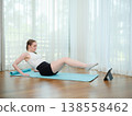 Young woman doing core exercise at home on yoga mat. Concept of fitness, strength training, and online workout. Female performing leg raise while following virtual fitness class. 138558462