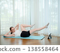 Young woman doing abdominal exercise at home on yoga mat. Concept of fitness, core training, and online workout. Female performing crunch while following virtual fitness class. 138558464