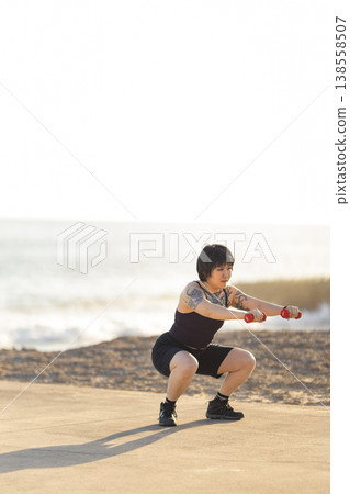 Woman squatting with dumbbells by ocean 138558507