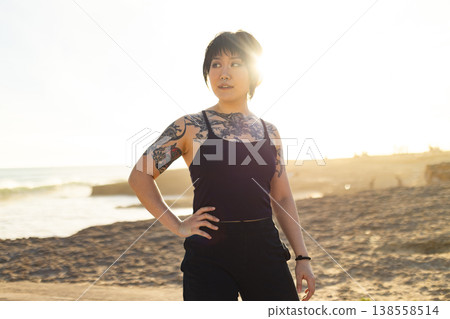 Young tattooed person standing on beach at sunset Young tattooed person standing on beach at sunset 138558514
