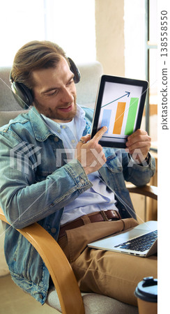 Man with headphones showing growth chart on tablet during online coaching. Man with headphones showing growth chart on tablet during online coaching. 138558550