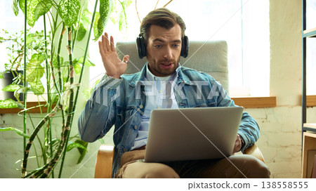Man with headphones reacting surprised during online coaching call on laptop. 138558555