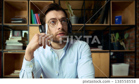 Man with headphones holding pen and looking up thinking in office interior. 138558558