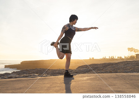 Young woman stretching leg on rocky coast at sunset Young woman stretching leg on rocky coast at sunset 138558846