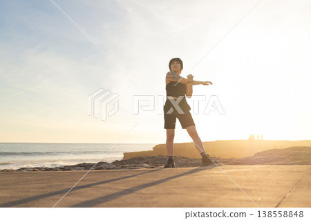 Woman stretching arm performing outdoor exercise at sunset 138558848
