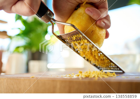 Hands grating lemon zest with metal grater on wooden board Hands grating lemon zest with metal grater on wooden board 138558859