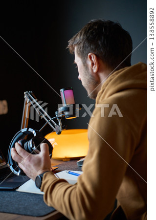 Man holding headphones near microphone in home podcast studio 138558892