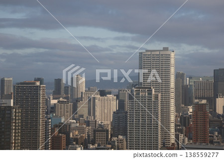 A view of Osaka's cityscape with clouds, blue sky, mountains, and clusters of skyscrapers. A view of Osaka's cityscape with clouds, blue sky, mountains, and clusters of skyscrapers. 138559277