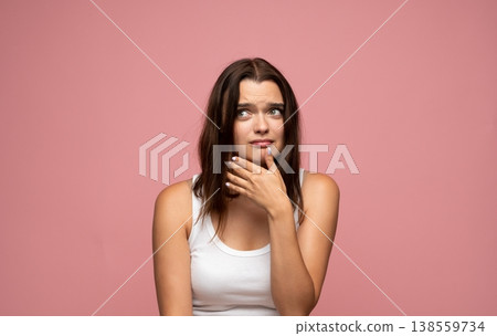 Young woman feeling doubt and uncertainty, looking away with worried expression on pink background Young woman feeling doubt and uncertainty, looking away with worried expression on pink background 138559734