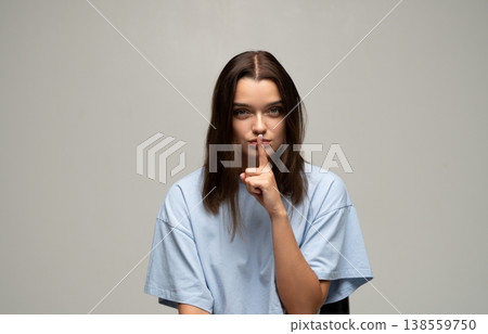 Young woman making a shush gesture, asking for quiet or keeping a secret. Serious expression, finger on lips Young woman making a shush gesture, asking for quiet or keeping a secret. Serious expression, finger on lips 138559750
