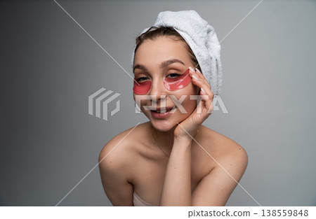 Young woman enjoying her at-home beauty routine, applying under-eye patches for skincare, wearing a towel on her head, embracing self-care and relaxation Young woman enjoying her at-home beauty routine, applying under-eye patches for skincare, wearing a towel on her head, embracing self-care and relaxation 138559848