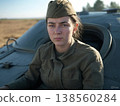 A young female soldier in a garrison cap gazes out of the hatch of a tactical vehicle, her eyes filled with quiet determination, out at the desolate landscape. 138560284