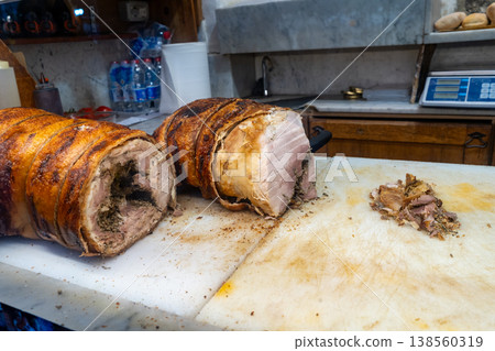 Two large cuts of roasted pork, one sliced, sit on a cutting board in a butcher shop with a scale in the background 138560319