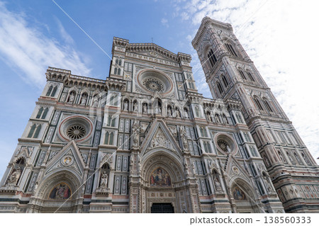 A low-angle view of the ornate facade of Florence Cathedral, also known as Cattedrale di Santa Maria del Fiore, and its adjacent bell tower, Giotto's Campanile, under a dynamic sky A low-angle view of the ornate facade of Florence Cathedral, also known as Cattedrale di Santa Maria del Fiore, and its adjacent bell tower, Giotto's Campanile, under a dynamic sky 138560333