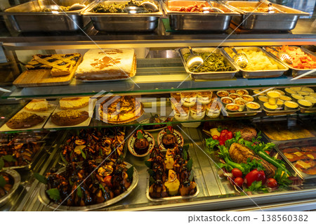 A refrigerated display case filled with a variety of sweet pastries, cakes, and savory prepared foods ready for service A refrigerated display case filled with a variety of sweet pastries, cakes, and savory prepared foods ready for service 138560382