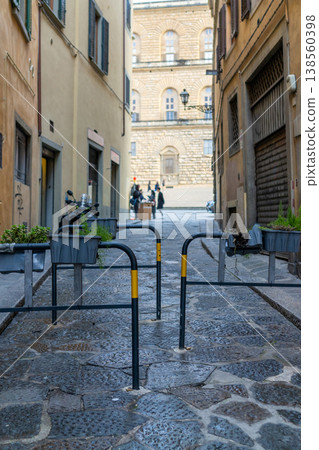 A view down a narrow, wet cobblestone street lined with old buildings and planters, leading to a grand facade in the distance A view down a narrow, wet cobblestone street lined with old buildings and planters, leading to a grand facade in the distance 138560398