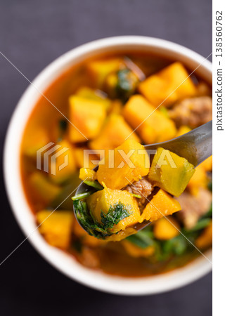 Thai spicy pumpkin curry soup with pork in a bowl scooping by spoon and eating Thai spicy pumpkin curry soup with pork in a bowl scooping by spoon and eating 138560762
