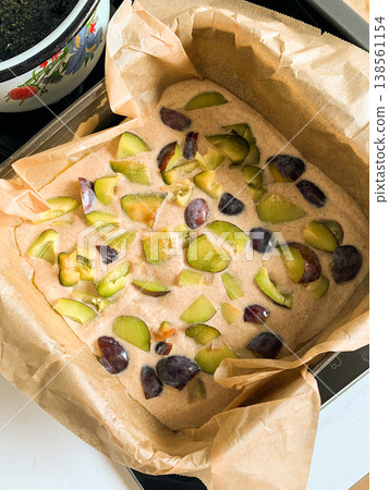 A person prepares gluten-free plum pie in a kitchen. The pie batter is filled with pieces of fresh plums. Bright colors of fruit stand out against a simple background 138561154