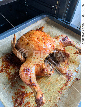 A whole chicken is placed in the oven. The dish is being cooked for dinner. The kitchen is warm and smells delicious as the food bakes A whole chicken is placed in the oven. The dish is being cooked for dinner. The kitchen is warm and smells delicious as the food bakes 138561197