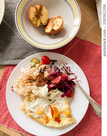 A plate holds an omelet topped with fermented cabbage, tomatoes, radish, and cucumbers alongside a baked apple. This scene showcases a healthy breakfast in a home kitchen A plate holds an omelet topped with fermented cabbage, tomatoes, radish, and cucumbers alongside a baked apple. This scene showcases a healthy breakfast in a home kitchen 138561204