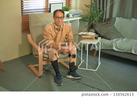 Confident middle-aged man wearing a prosthetic leg sitting at home Confident middle-aged man wearing a prosthetic leg sitting at home 138562613
