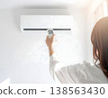 A woman in white clothes holding an air conditioner remote control. 138563430