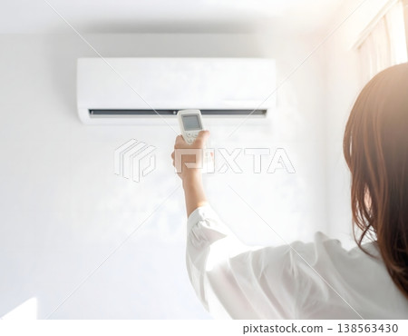 一名身穿白衣的女子手持空調遙控器。 一名身穿白衣的女子手持空調遙控器。 138563430