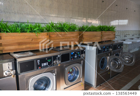 Modern laundromat interior with row of washing machines and wooden planters with green plants clean self service laundry concept 138563449