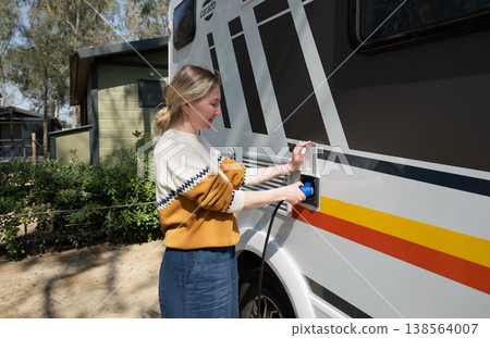Woman connecting power cable to motorhome campervan at campsite electric hookup travel lifestyle concept 138564007