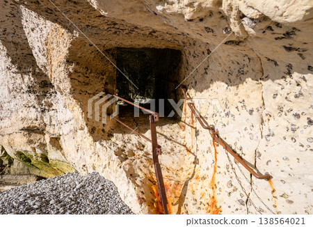 Ancient coastal cave entrance with rusty metal railing in limestone cliff seaside exploration concept 138564021