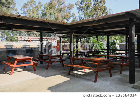 Wooden picnic tables under covered shelter in campsite park outdoor dining area travel and leisure concept Wooden picnic tables under covered shelter in campsite park outdoor dining area travel and leisure concept 138564034