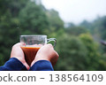 Close up Hand holding a glass cup of hot coffee in green natural background. Copy space 138564109