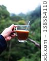 Close up Hand holding a glass cup of hot coffee in green natural background. Copy space 138564110