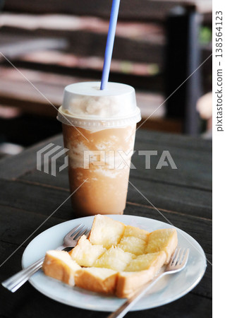 Homemade toast or bread with butter topping in white dish with blended latte coffee in plastic glass on wooden table 138564123