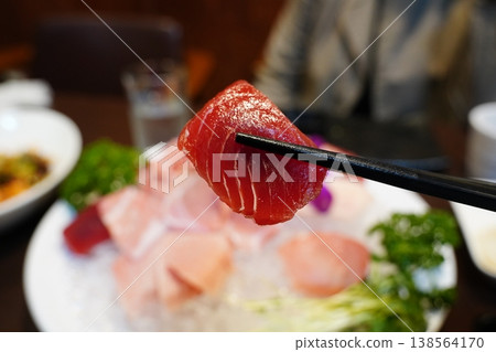 close-up photo of a piece of fresh tuna sashimi picked up with chopsticks. 138564170