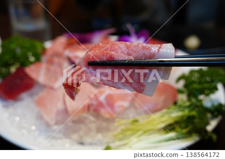 close-up photo of a piece of fresh tuna sashimi picked up with chopsticks. 138564172