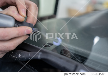 A technician drills a hole during a car windshield chip repair. A technician drills a hole during a car windshield chip repair. 138564583