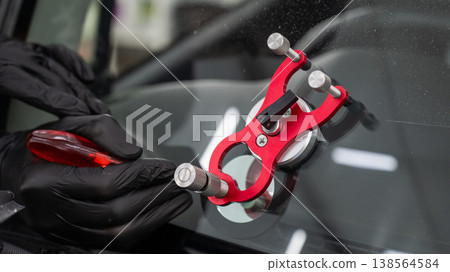 A technician injects resin into a windshield crack. A technician injects resin into a windshield crack. 138564584
