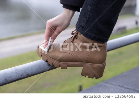 Person's hand cleaning a brown combat boot with a wet wipe on an outdoor railing, emphasizing quick shoe care and personal hygiene Person's hand cleaning a brown combat boot with a wet wipe on an outdoor railing, emphasizing quick shoe care and personal hygiene 138564592