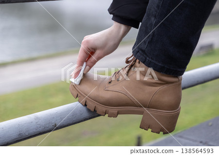 Woman's hand meticulously cleans a sturdy brown leather boot using a white disposable wipe, highlighting practical outdoor shoe care and proactive footwear maintenance Woman's hand meticulously cleans a sturdy brown leather boot using a white disposable wipe, highlighting practical outdoor shoe care and proactive footwear maintenance 138564593