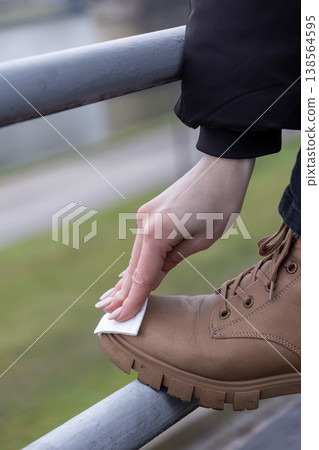 Person's hand diligently cleans a sturdy brown hiking boot with a white wipe, emphasizing responsible outdoor gear maintenance and preparation 138564595
