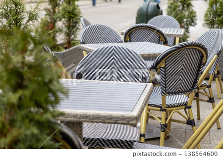 Stylish outdoor cafe furniture featuring patterned black and white chairs, modern tables, ready for urban sidewalk dining, promoting relaxed leisure 138564600