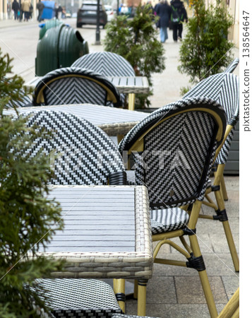 Empty urban street cafe dining area displays black and white chevron chairs and rattan tables, inviting city dwellers for relaxation and social gathering Empty urban street cafe dining area displays black and white chevron chairs and rattan tables, inviting city dwellers for relaxation and social gathering 138564647