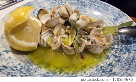 Cooked cockles in garlic butter with lemon wedge on blue patterned plate for spanish tapas seafood starter and sharing dish. Cockle, Cardiidae Cooked cockles in garlic butter with lemon wedge on blue patterned plate for spanish tapas seafood starter and sharing dish. Cockle, Cardiidae 138564670