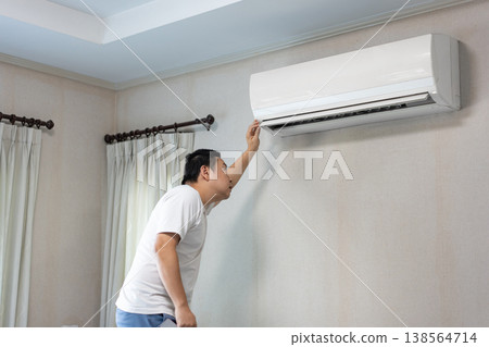 Home Maintenance and Air Conditioner Check, A man inspects an air conditioner at home, checking its performance as part of regular household maintenance. Home Maintenance and Air Conditioner Check, A man inspects an air conditioner at home, checking its performance as part of regular household maintenance. 138564714