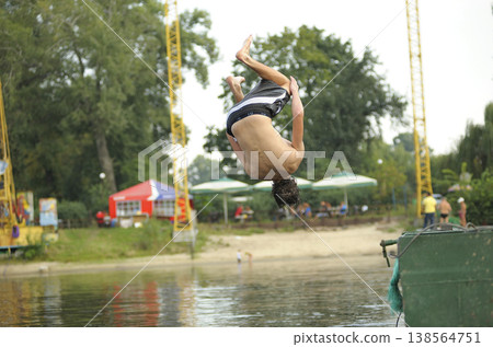 Young man doing a backflip into the river from a pier on a summer beach 138564751