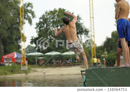 Young man doing a backflip into the river from a pier on a summer beach Young man doing a backflip into the river from a pier on a summer beach 138564753